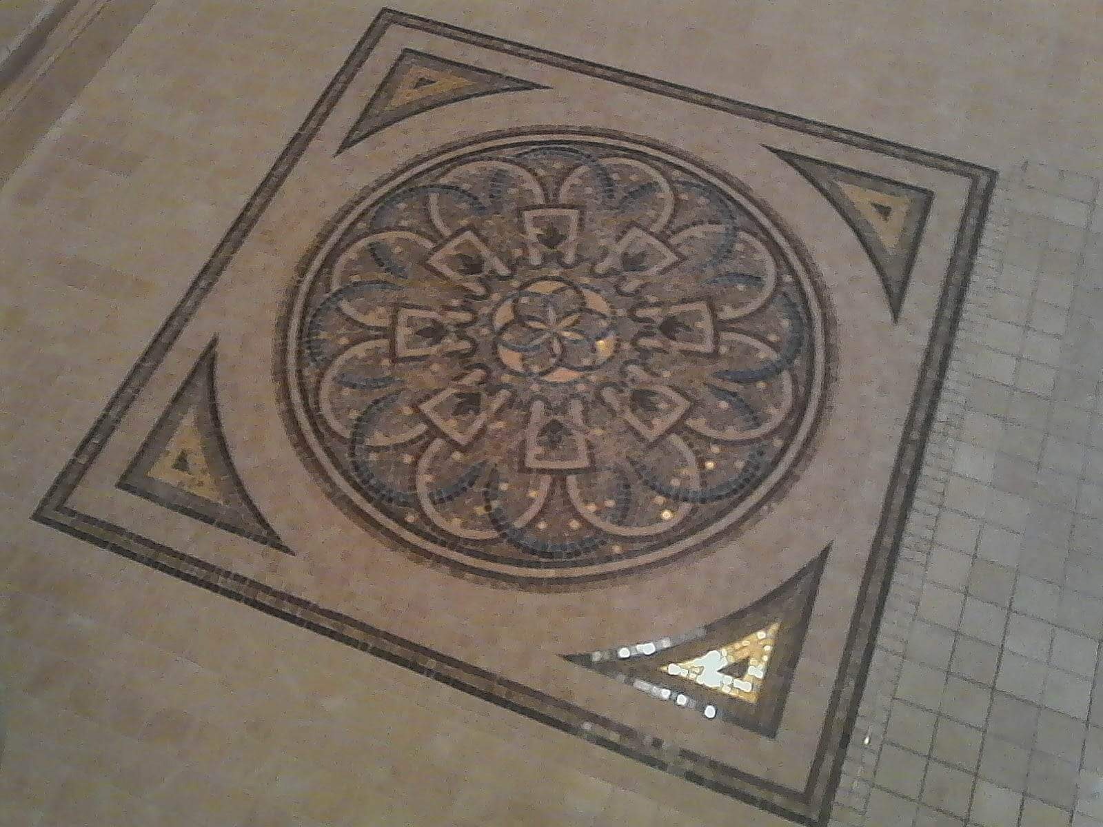 Dekoracyjna mozaika podłogowa w odcieniach beżu i brązu, z geometrycznym wzorem rozetowym w centrum kwadratowej ramy.