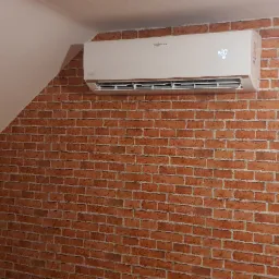 Biała jednostka klimatyzacyjna Viessmann zamontowana na ścianie z cegieł w pokoju na poddaszu, wyświetlająca temperaturę 20 stopni Celsjusza.