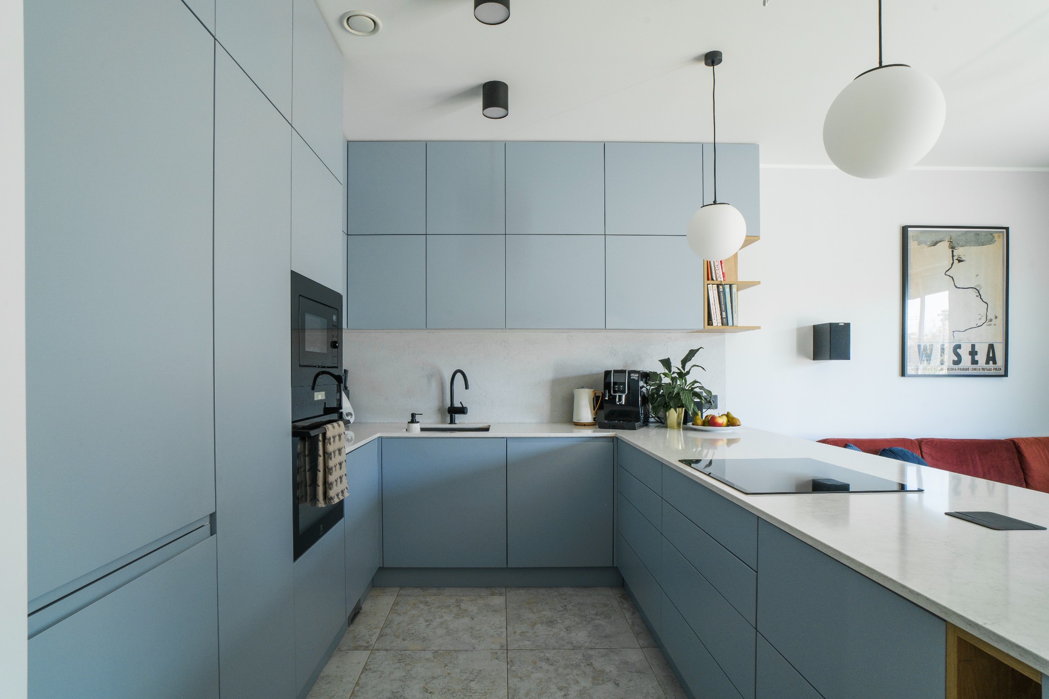 Nowoczesna kuchnia w odcieniach szarości z matowymi frontami, białym blatem i czarną armaturą, oświetlona wiszącymi lampami kulami i punktowymi reflektorami.