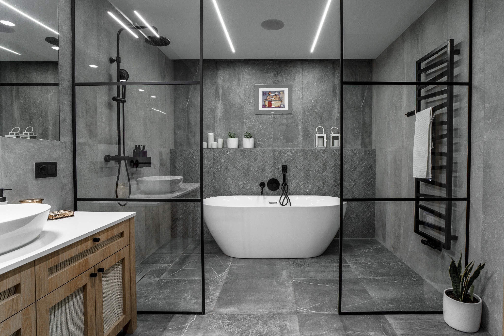 Nowoczesna łazienka w odcieniach szarości z wolnostojącą białą wanną, przeszkloną kabiną prysznicową z czarną armaturą i drewnianą szafką pod umywalką.