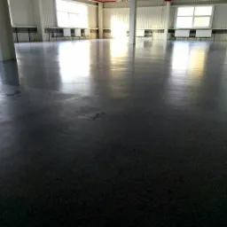 Błyszcząca, szara posadzka przemysłowa w hali z oknami i białymi kolumnami, odbijająca światło.