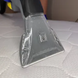 Dysza czyszcząca odkurzacza piorącego na białym materacu podczas procesu czyszczenia, widoczne niebieskie rękawice