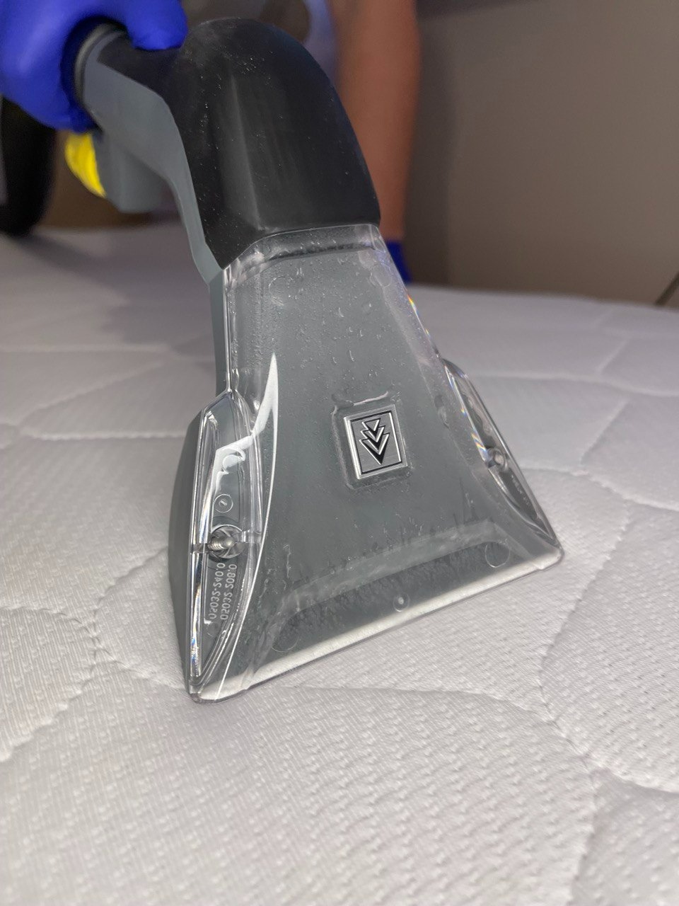 Dysza czyszcząca odkurzacza piorącego na białym materacu podczas procesu czyszczenia, widoczne niebieskie rękawice