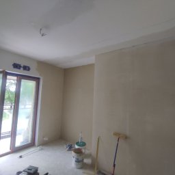 Marmulewski - Wnętrze w trakcie prac przygotowawczych do malowania: ściany pokryte gładzią, widoczne narzędzia malarskie, otwarte okno balkonowe z widokiem na zieleń.