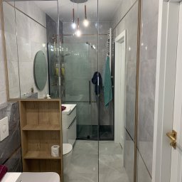 Zakład Stolarsko Budowlany HOLZ Rafał Bembnowicz - Nowoczesna łazienka z lustrzanymi drzwiami, szare płytki z marmurkowym wzorem i drewniane półki obok toalety. Widoczna kabina prysznicowa z czarnymi elementami i wisząca lampa z trzema żarówkami.