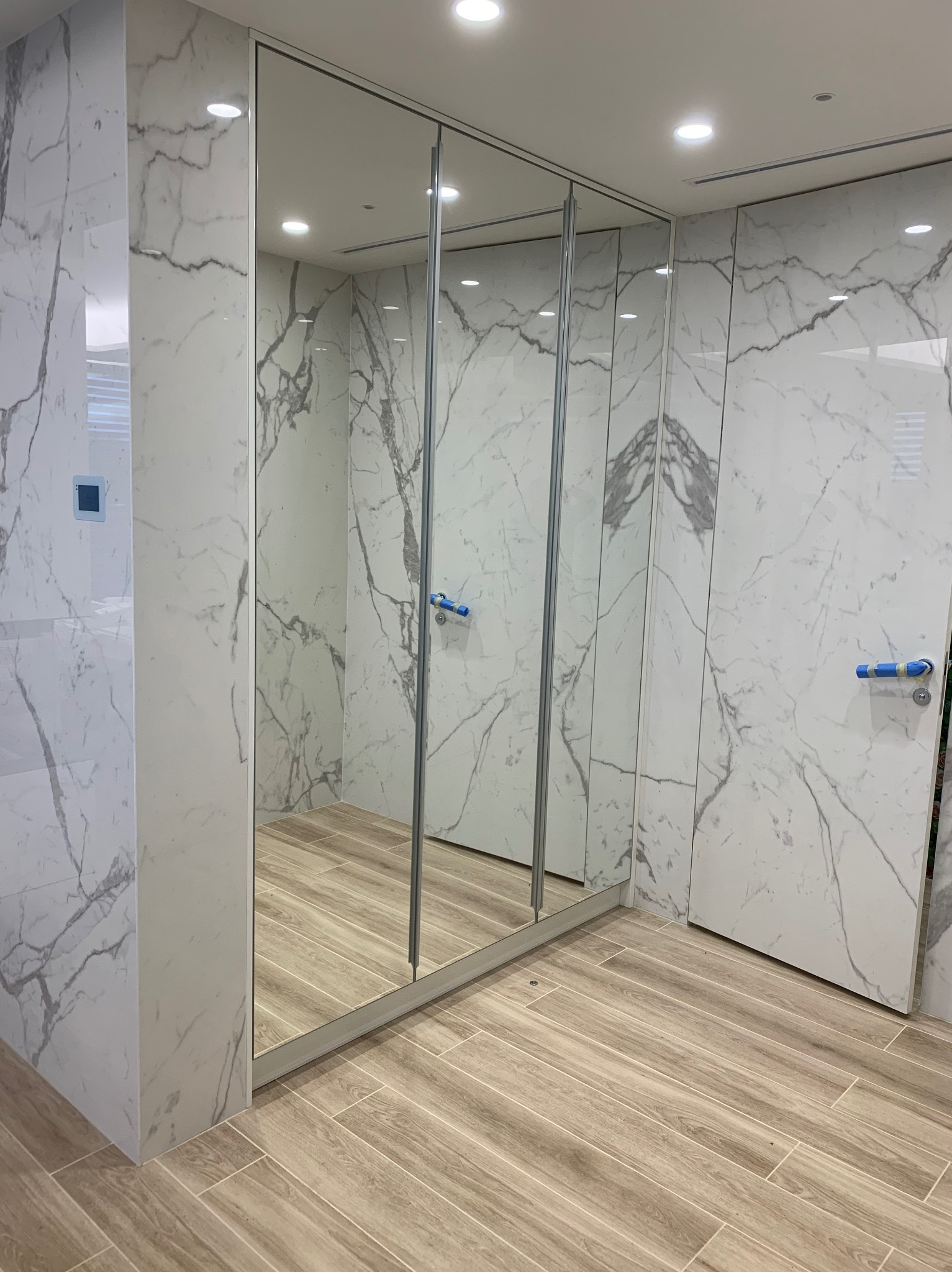 Nowoczesna szafa wnękowa z lustrzanymi drzwiami przesuwnymi i wykończeniem imitującym marmur, z widocznymi fragmentami wnętrza odbijającymi się w lustrze.