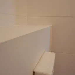 Fragment narożnika wykończonego płytami kartonowo-gipsowymi, widoczna krawędź płyty z nacięciami, przygotowana do zaginania i łączenia, na jasnym tle ściany.