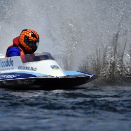 Artur Pawlak - Motorówka w pełnym biegu, pilot w pomarańczowym kasku, woda rozpryskuje się dookoła, widoczny numer 46 i nazwa zespołu 'floodule POWERBOAT RACING TEAM'.
