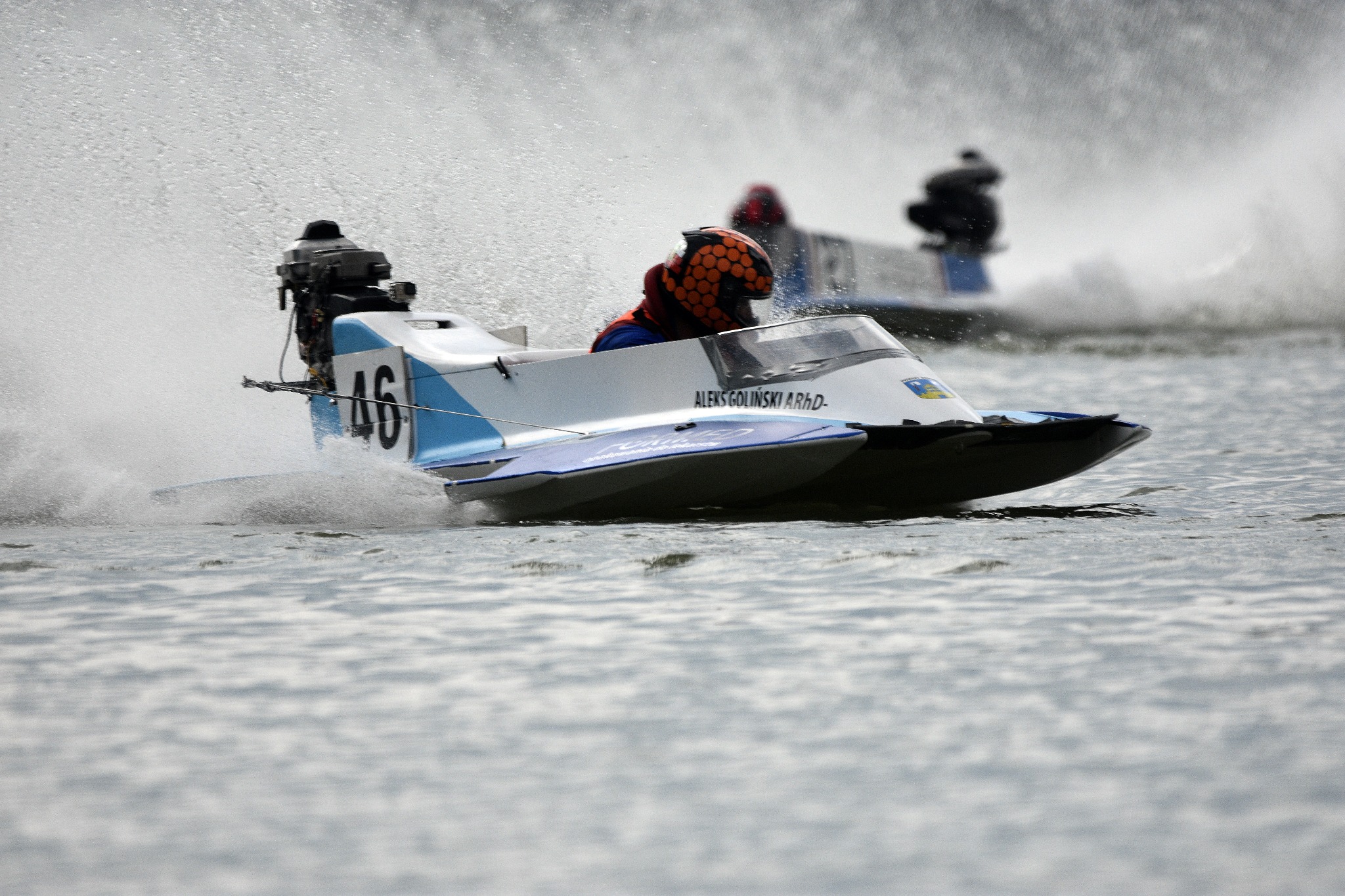 Motorówka wyścigowa z numerem 46, pędząca po wodzie, w tle inne łodzie i fontanny wody.