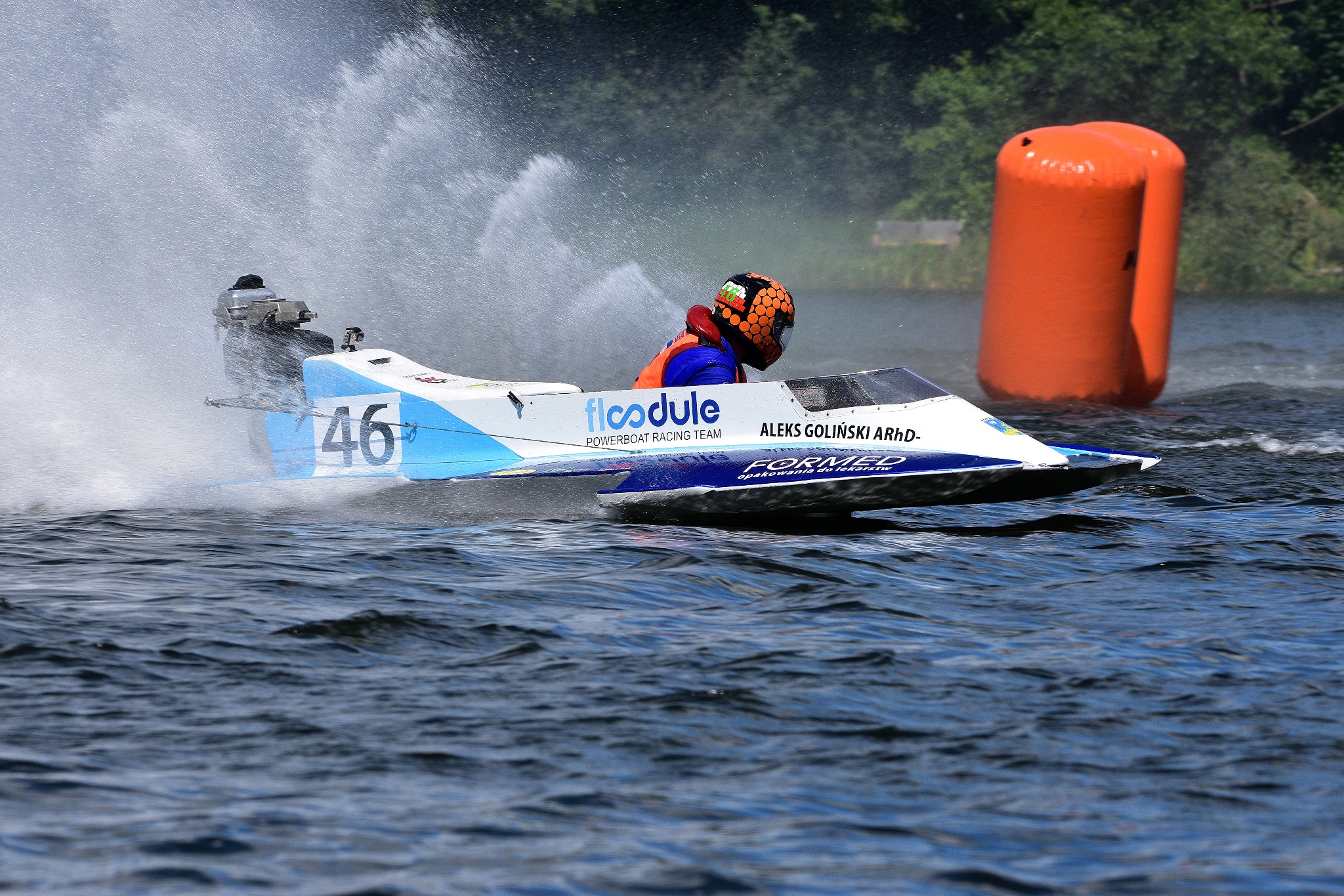 Łódź motorowa z numerem 46 ścigająca się na wodzie, w tle pomarańczowa boja i zieleń drzew.