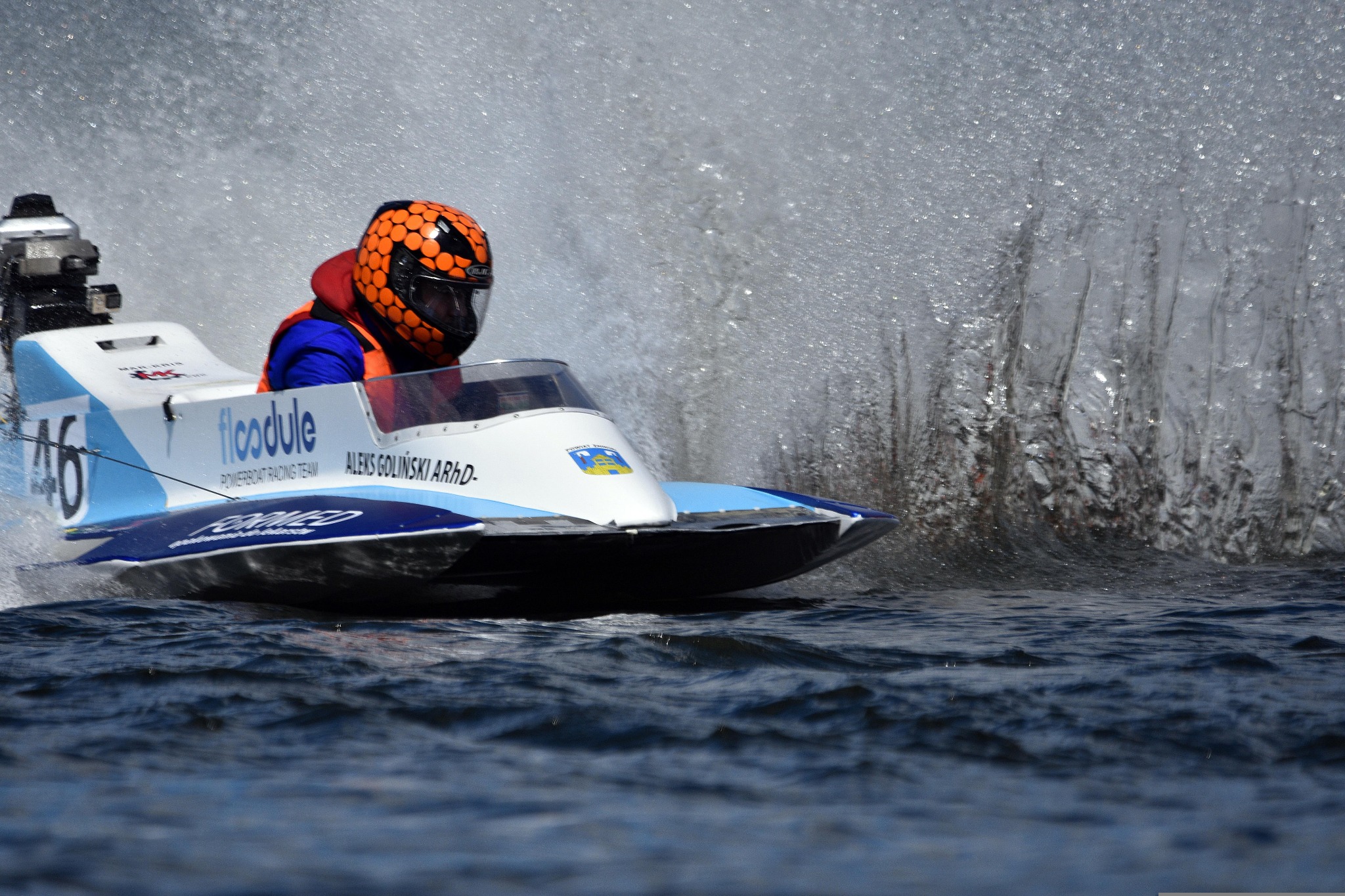 Motorówka w pełnym biegu, pilot w pomarańczowym kasku, woda rozpryskuje się dookoła, widoczny numer 46 i nazwa zespołu 'floodule POWERBOAT RACING TEAM'.