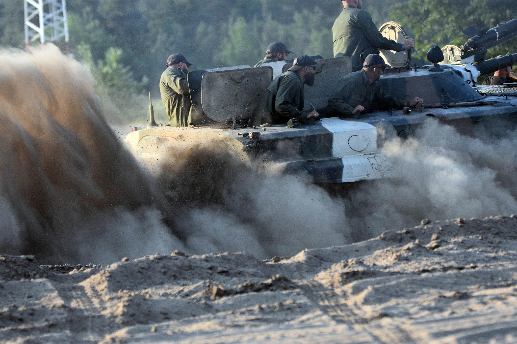 Grupa żołnierzy w wojskowym pojeździe opancerzonym pokonuje piaszczysty teren, wzbijając tumany kurzu.