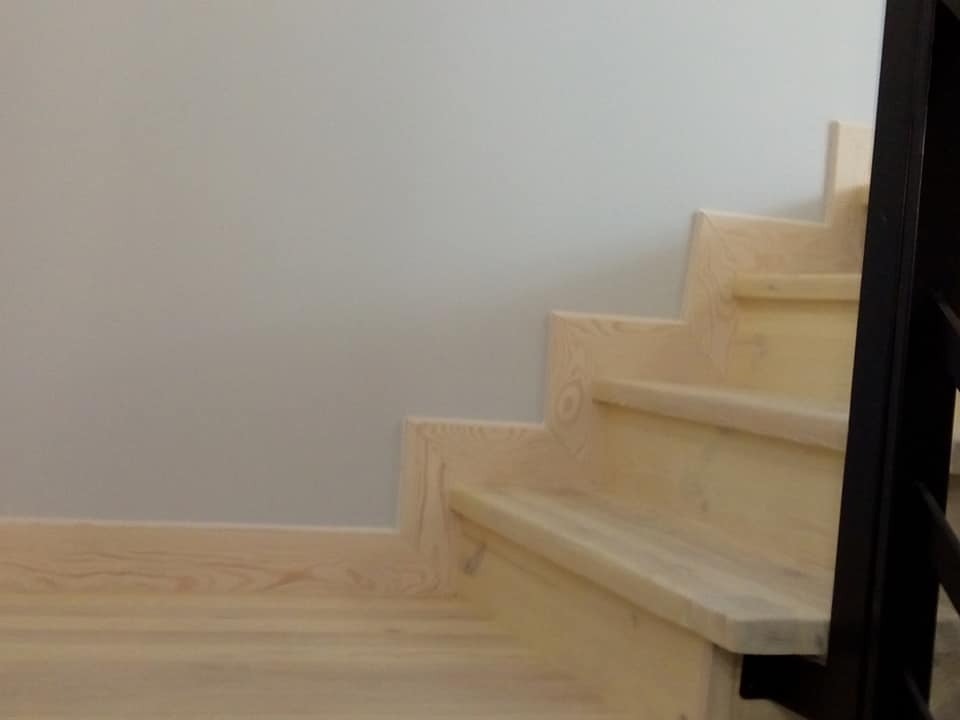 Jasne drewniane schody z czarną balustradą, widok z dołu, świeżo po renowacji, z widoczną strukturą drewna i gładką powierzchnią.