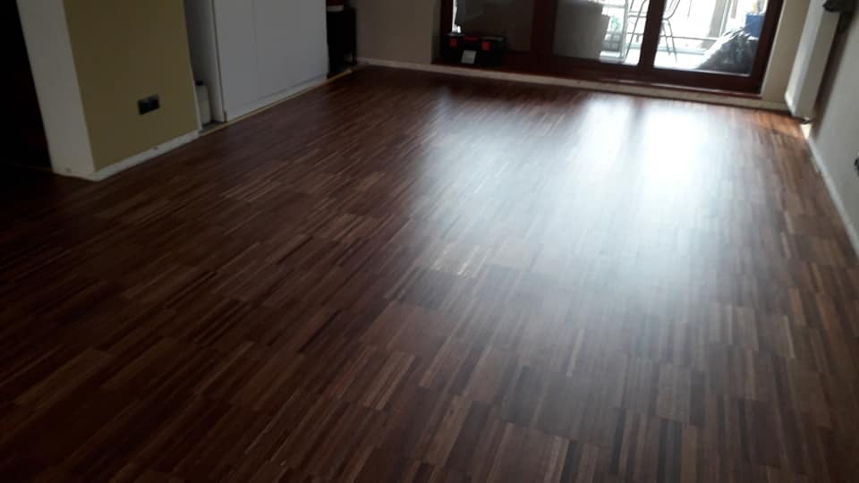 Ułożony parkiet z ciemnego drewna w nowym mieszkaniu, widoczne przesuwne drzwi balkonowe i skrzynka z narzędziami w tle.