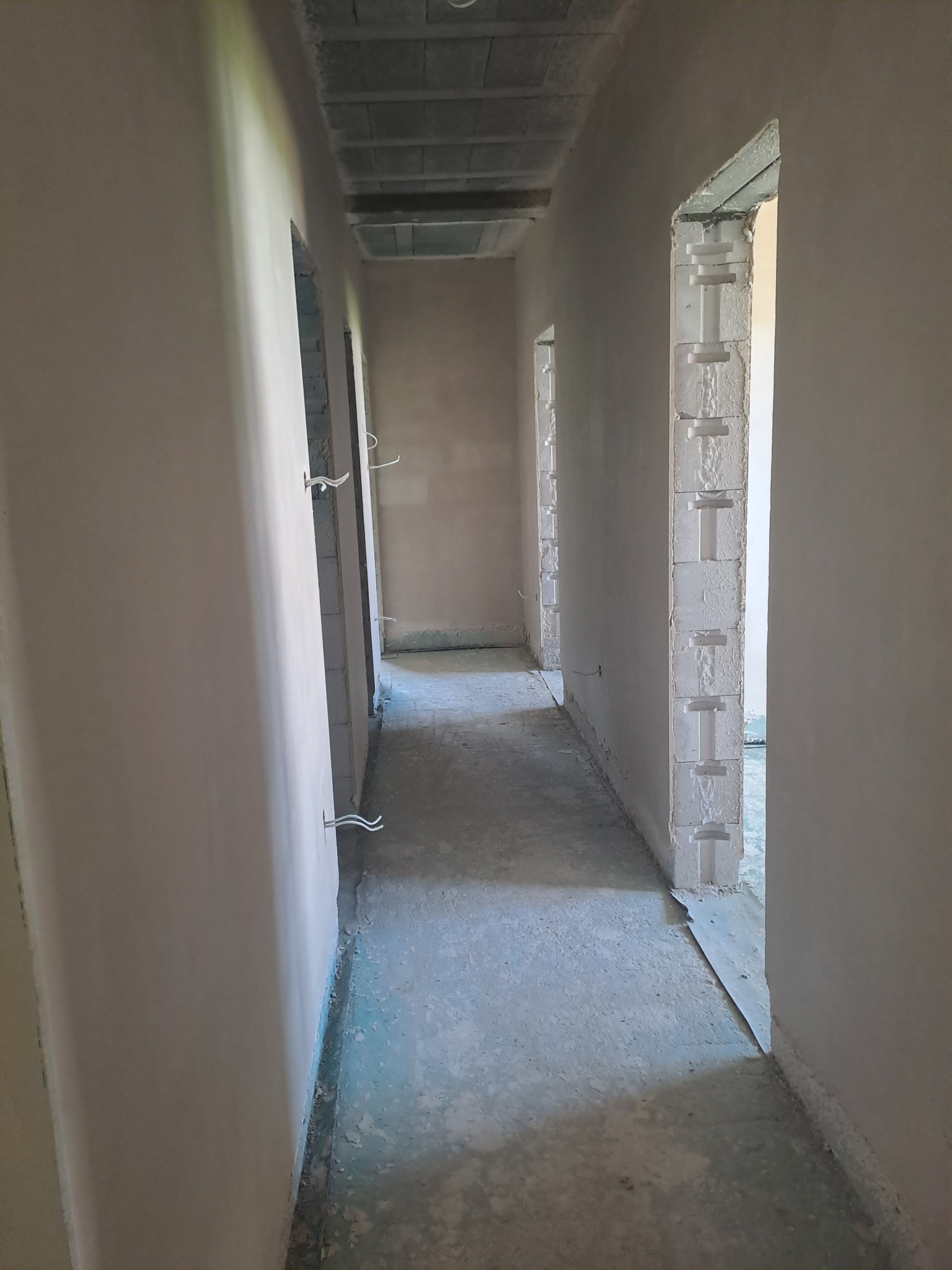 Korytarz w surowym stanie po nałożeniu tynków w Przewodowie. Widoczne ściany po tynkowaniu i otwory drzwiowe z elementami konstrukcyjnymi z betonu komórkowego.