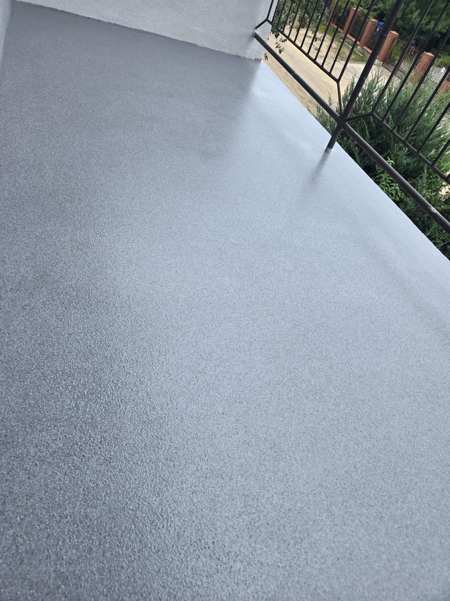 Szara, gładka posadzka na balkonie z metalową balustradą, widok z góry. Nowoczesne wykończenie, równa powierzchnia, świeżo położona.