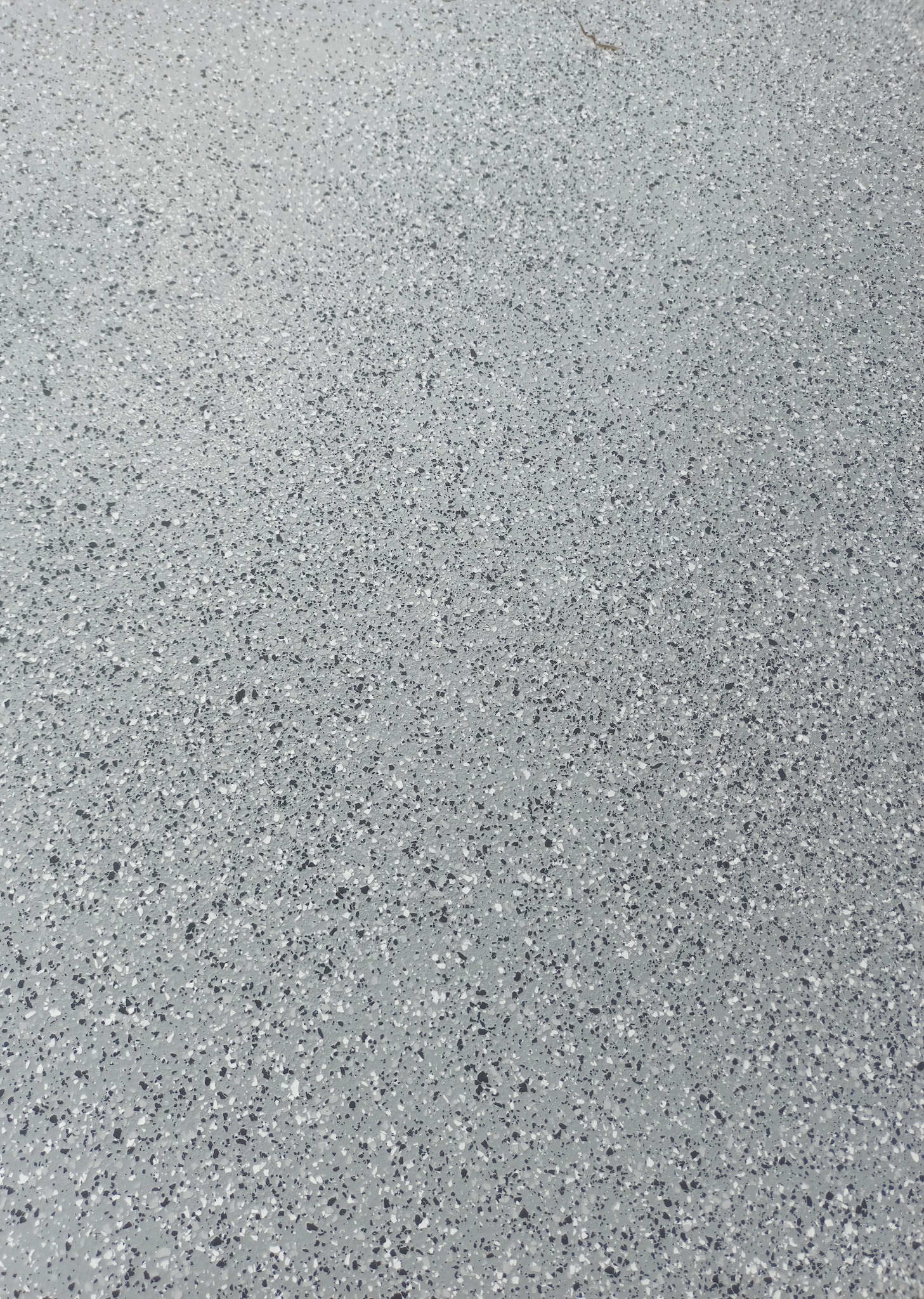 Szara posadzka z drobnymi, nieregularnymi plamkami w odcieniach bieli i czerni, tworząca jednolitą, gładką powierzchnię. Widok z góry, bez widocznych krawędzi.