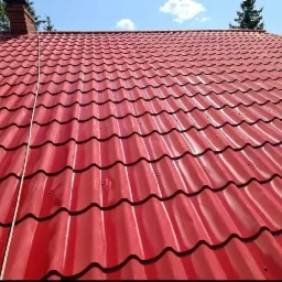 Czerwony dach z blachodachówki modułowej, widoczny komin z cegły, błękitne niebo w tle