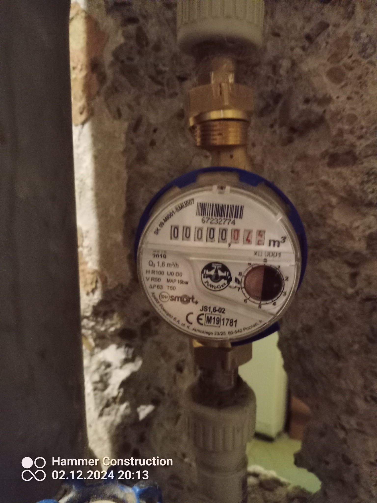 Zamknięty kadr na licznik wody z widocznym wskazaniem 0000045 m3, zamontowany na rurach w ścianie z surowego betonu.