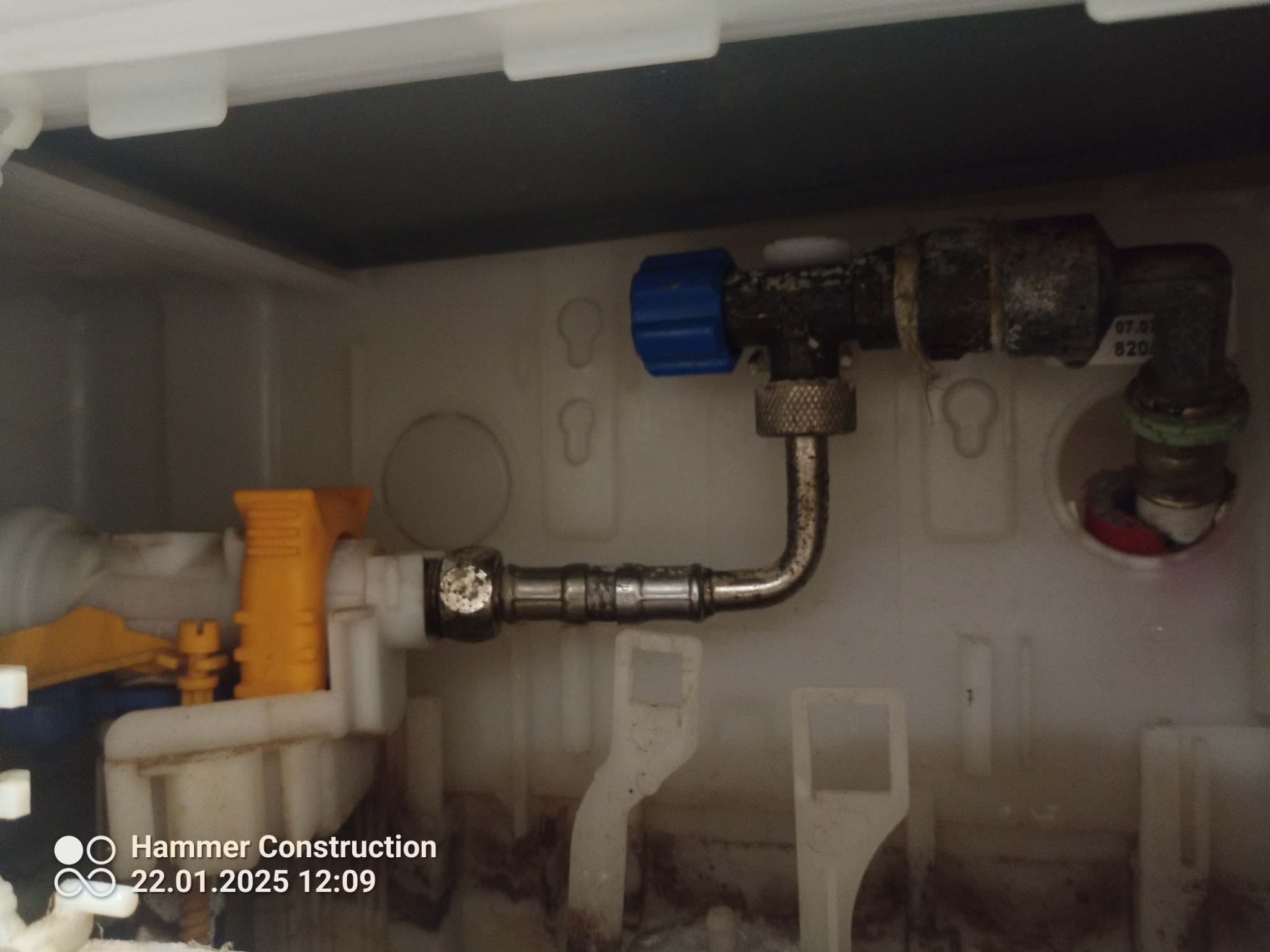 Wnętrze spłuczki WC z widocznymi elementami instalacji wodnej, armaturą z niebieskim zaworem i żółtym mechanizmem spustowym, widoczne ślady użytkowania.