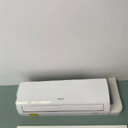 Biała jednostka klimatyzacji Sinclair zamontowana pod sufitem, widoczna z dołu, z fragmentem zielonej ściany i białej futryny drzwiowej.