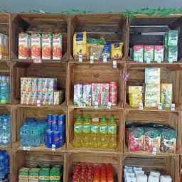 Regał sklepowy z drewnianych skrzynek wypełniony r&oacute;żnorodnymi produktami spożywczymi, napojami, kawami, herbatami, olejami i przyprawami, z cenami umieszczonymi przy każdym produkcie.