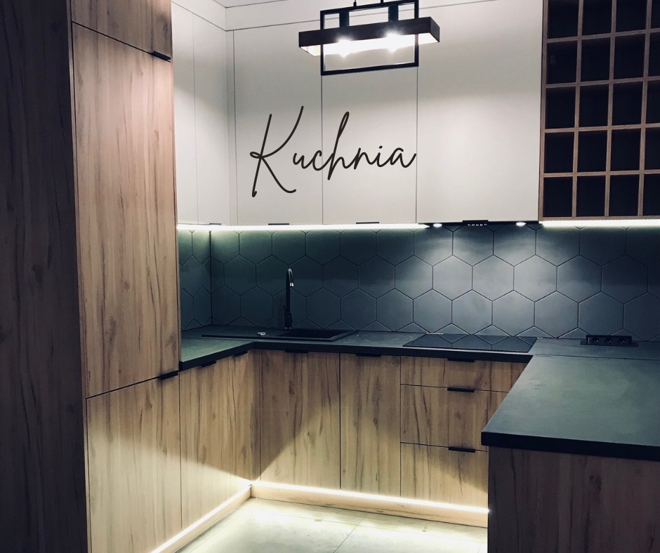 Nowoczesna kuchnia z drewnianymi frontami szafek dolnych i białymi górnymi, heksagonalne płytki na ścianie, czarny zlew i bateria, oświetlenie LED pod szafkami, dekoracyjny napis 'Kuchnia' na ścianie.