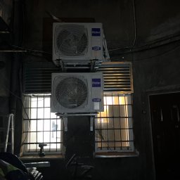 Smart Free Wind - Dwa klimatyzatory Haier zamontowane jeden nad drugim na elewacji budynku, widoczne okna z kratami i wiertarka na parapecie, słabe oświetlenie
