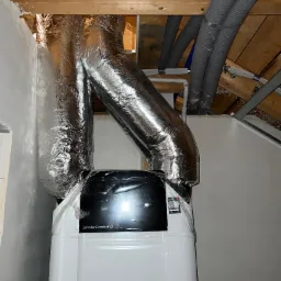 Zainstalowany centralny system wentylacji mechanicznej z odzyskiem ciepła Zehnder ComfoAir Q z izolowanymi przewodami wentylacyjnymi w przestrzeni poddasza, widoczne rury szare i niebieskie.