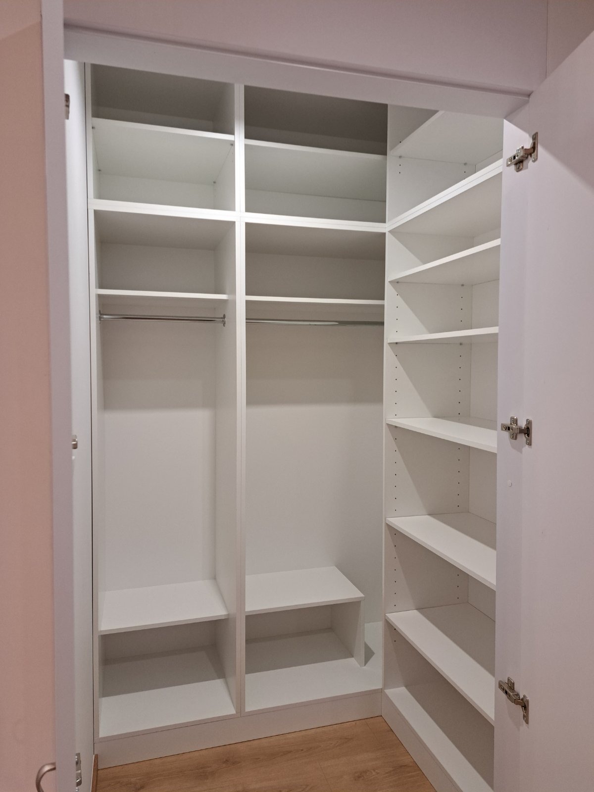 Wnętrze przestronnej, białej szafy wnękowej z otwartymi drzwiami, widoczne półki, drążki na ubrania i dolne schowki, na podłodze panele imitujące drewno.