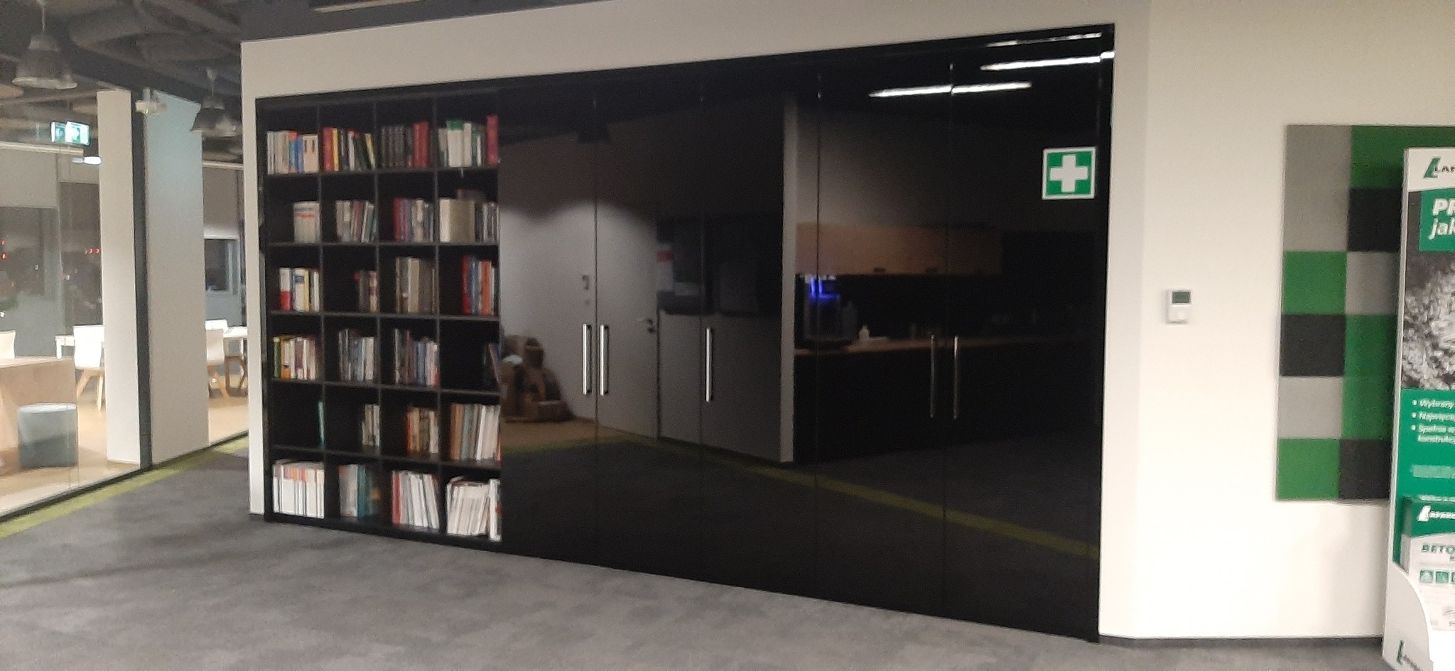 Nowoczesna, czarna zabudowa z regałem na książki, szklanymi drzwiami przesuwnymi z uchwytami i elementami biurowymi widocznymi w tle.