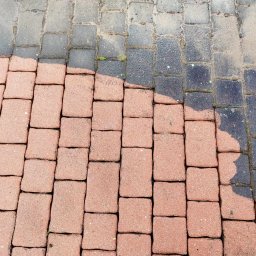 Usługi Sprzątające MKG - Częściowo umyta, czerwona kostka brukowa. Widoczna różnica w kolorze między czystą, a brudną kostką. W tle fragment węża ogrodowego.