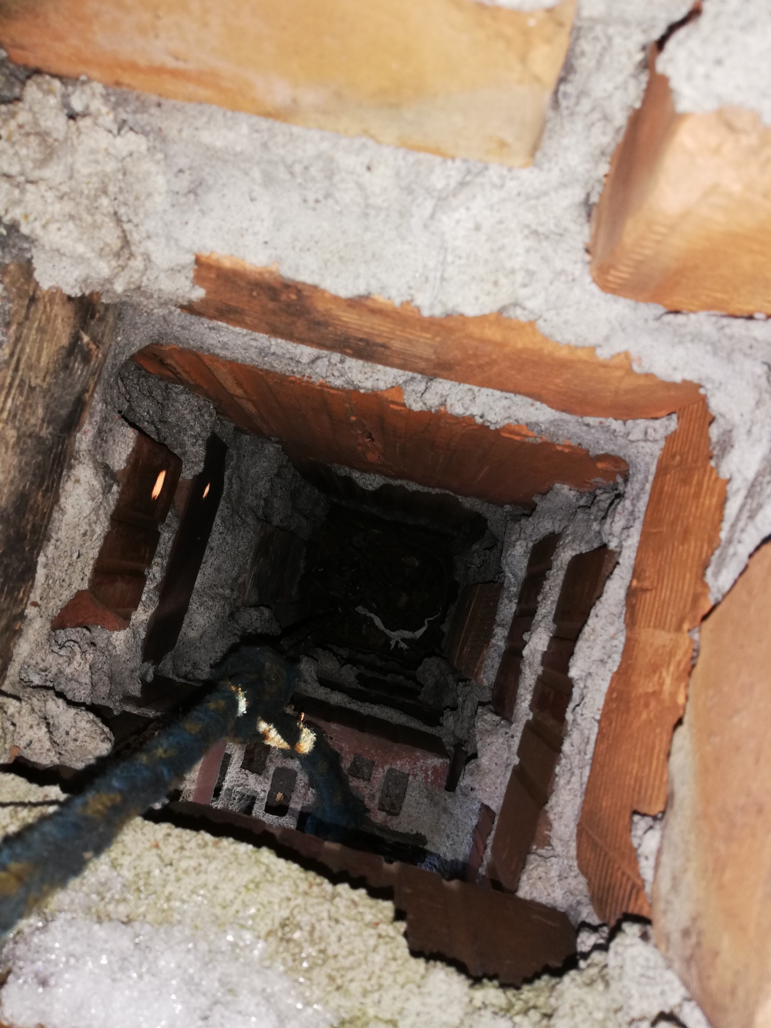 Wnętrze komina z cegły, widok z góry, z widoczną liną kominiarską i osadami sadzy.