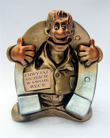 Figurka z brązu przedstawiająca uśmiechniętego mężczyznę w koszuli, trzymającego kciuki w górę, z napisem 'Chwytaj szczęście w swoje ręce' na kartce przyczepionej do koszuli.