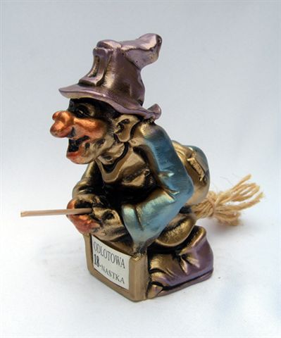 Gipsowa figurka wiedźmy na miotle, z tabliczką 'Odlotowa 18-nastka', malowana na złoto, fioletowo i niebiesko, na białym tle.