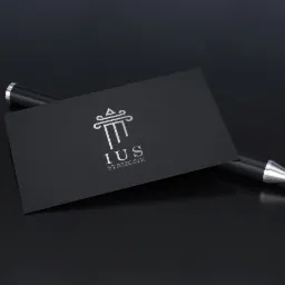 Elegancka wizytówka firmy prawniczej IUS Staszczyk z srebrnym logo kolumny na czarnym tle, obok leży czarny długopis.