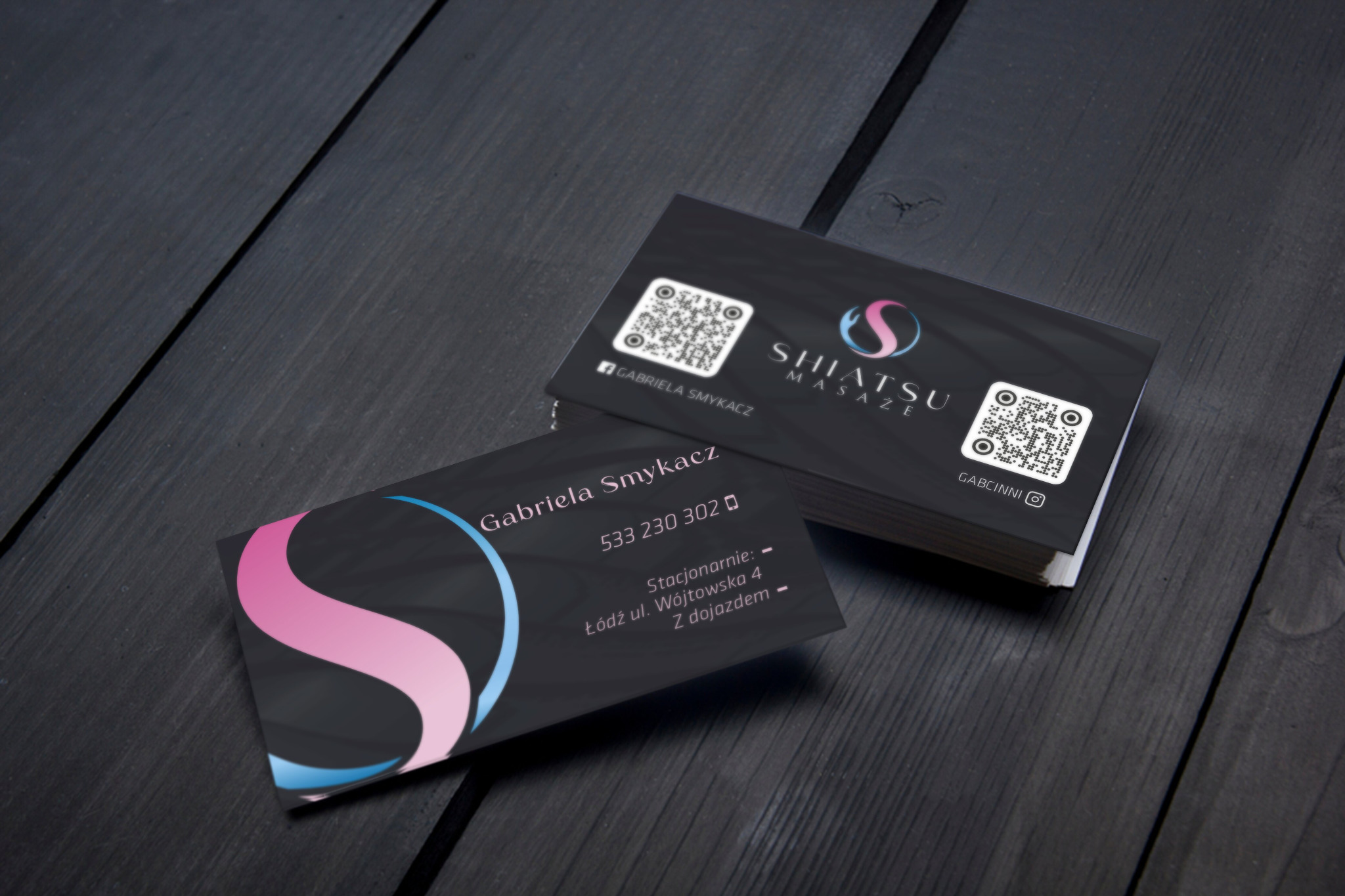 Stos wizytówek na ciemnym drewnianym tle, z logo Shiatsu Masaże i kodami QR.