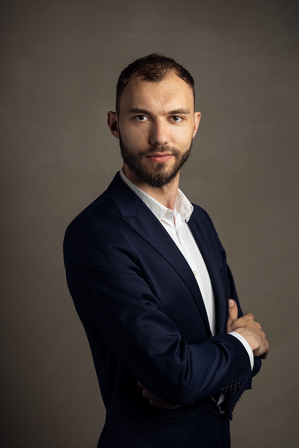 Portret mężczyzny w garniturze z Gdańska, z założonymi rękami, na neutralnym tle.