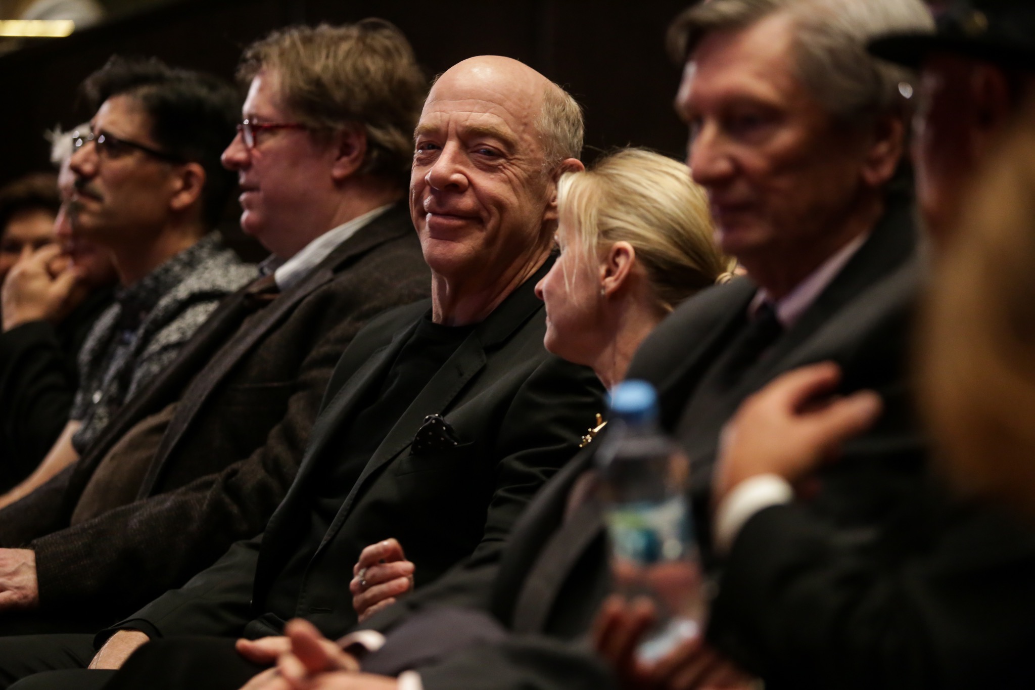 Widownia podczas wydarzenia kulturalnego, mężczyzna w czarnym garniturze spogląda w stronę obiektywu.