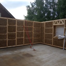 ecomodus - Wnętrze domu w trakcie budowy z paneli ze słomy i drewnianej konstrukcji, widoczne podpory i poziomica.