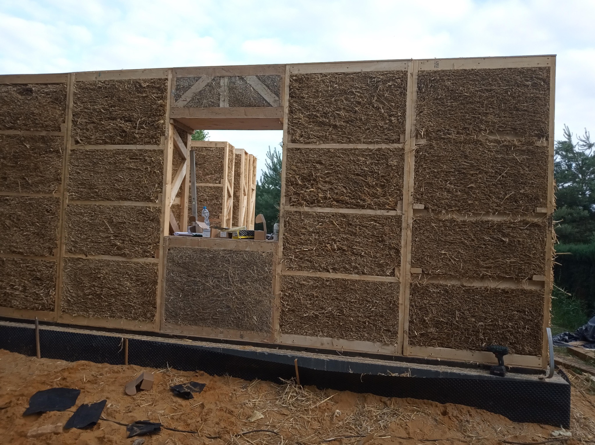 Budowa domu szkieletowego: ściana z paneli wypełnionych słomą w drewnianej ramie, widoczne narzędzia i materiały budowlane na placu budowy.