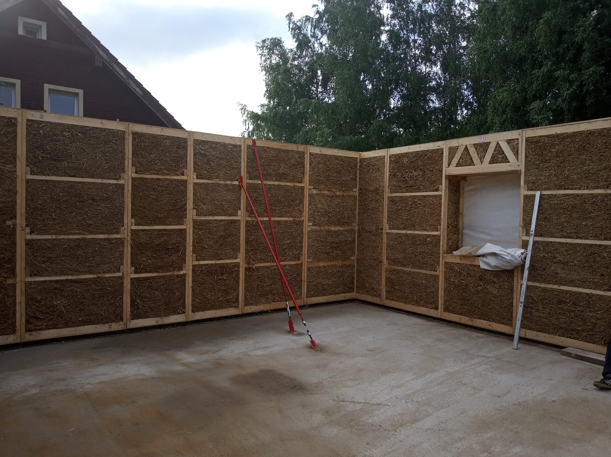 Wnętrze domu w trakcie budowy z paneli ze słomy i drewnianej konstrukcji, widoczne podpory i poziomica.