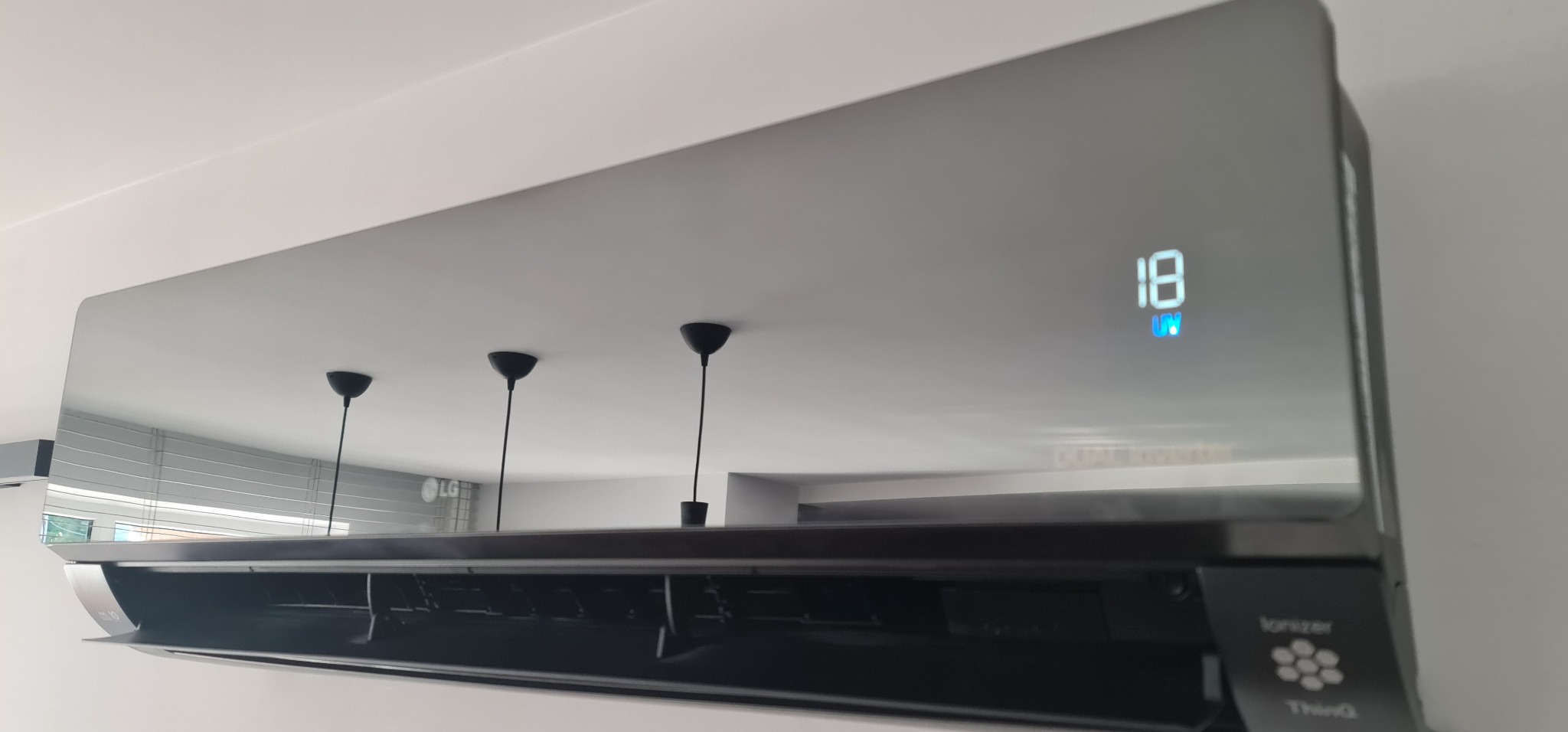 Błyszczący, czarny klimatyzator LG zamontowany na białej ścianie, z widocznym wyświetlaczem temperatury i odbiciem lamp w obudowie.