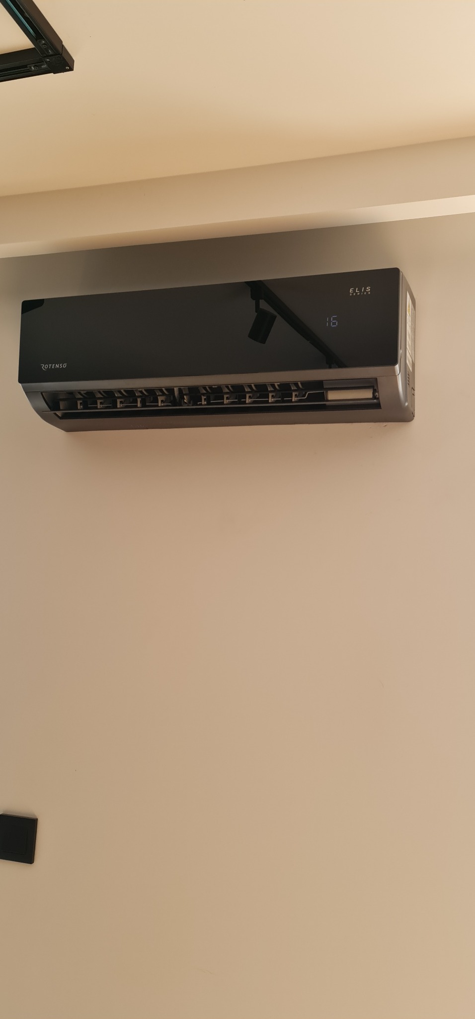 Czarny klimatyzator Rotenso Elis Series zamontowany na beżowej ścianie, wyświetlający temperaturę 16 stopni Celsjusza.