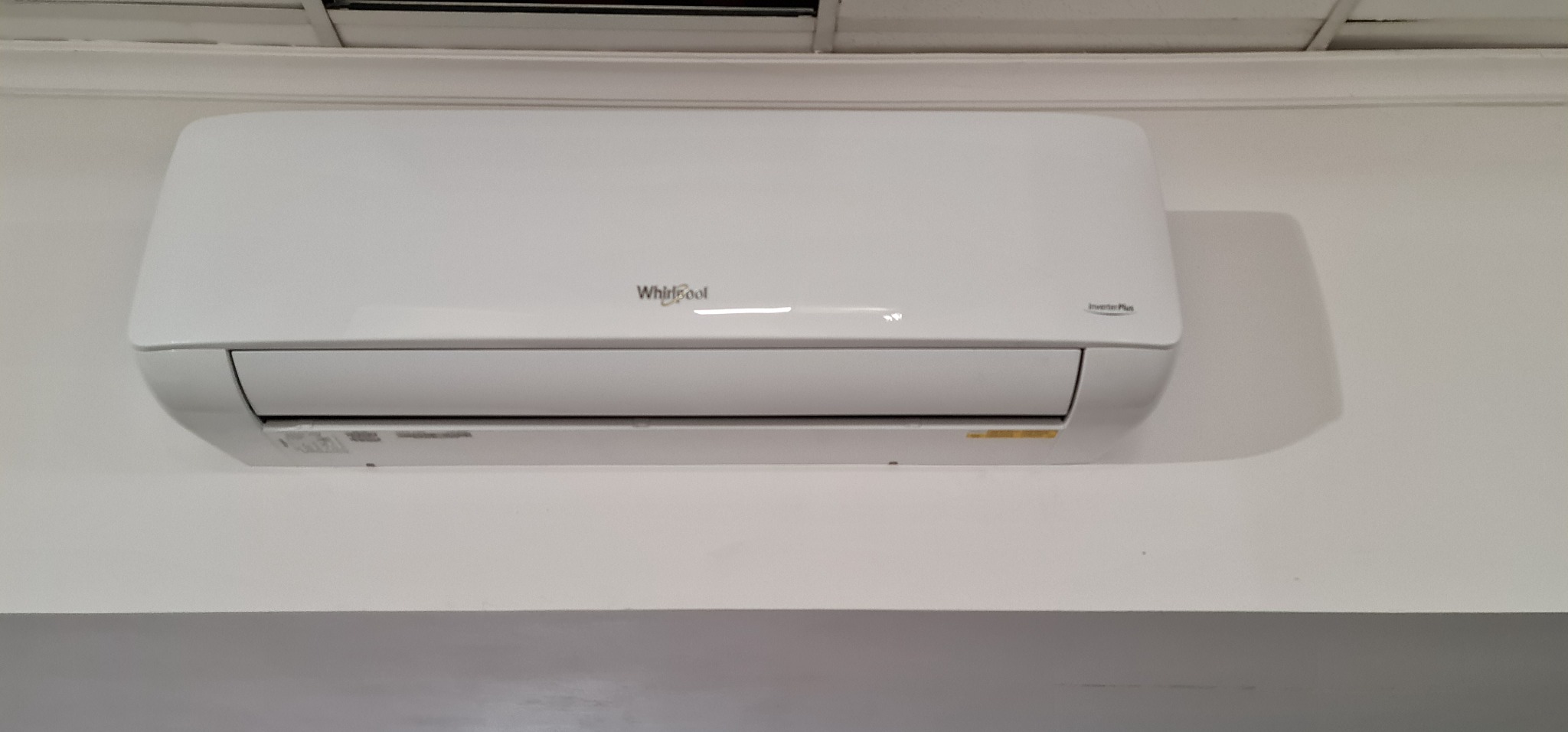 Biała klimatyzacja Whirlpool Inverter Plus zamontowana na białej ścianie w pomieszczeniu.