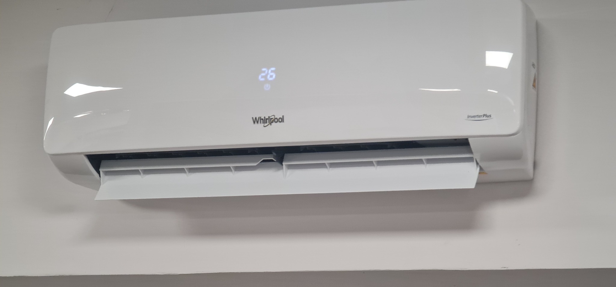 Biała jednostka klimatyzacyjna Whirlpool Inverter Plus zamontowana na ścianie, wyświetlająca temperaturę 26 stopni Celsjusza.