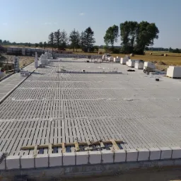 Fundament domu z pustaków szalunkowych na ażurowej płycie fundamentowej, widok z góry na plac budowy w słoneczny dzień.