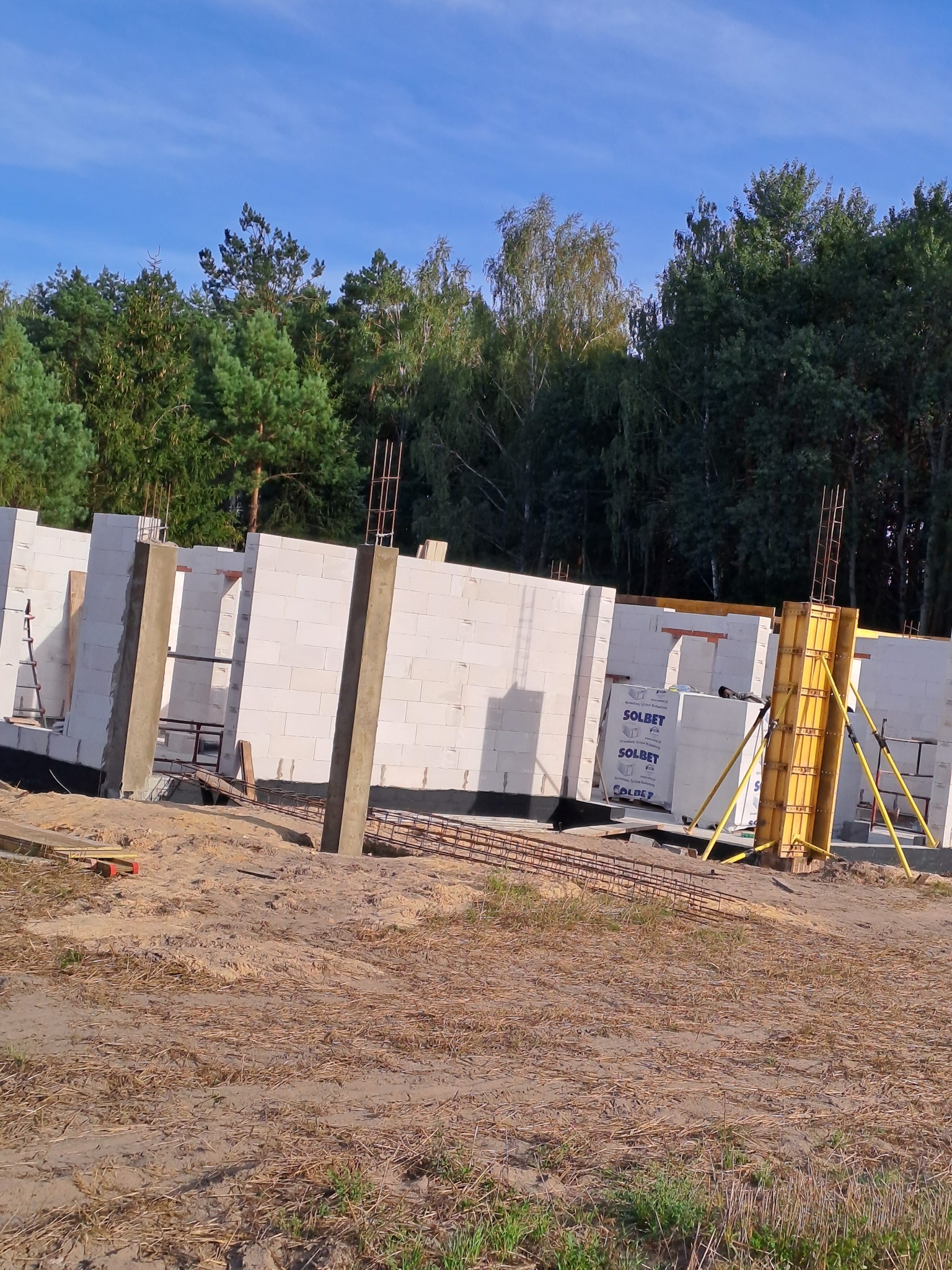 Wznoszenie ścian domu z bloczków Solbet, widoczne zbrojenia i szalunki, w tle las.