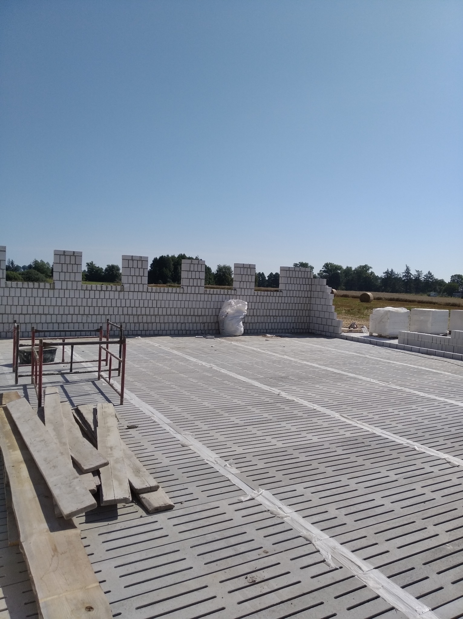 Wznoszenie ścian z bloczków z betonu komórkowego na ażurowym fundamencie, widoczne rusztowanie pomocnicze i bale drewniane.