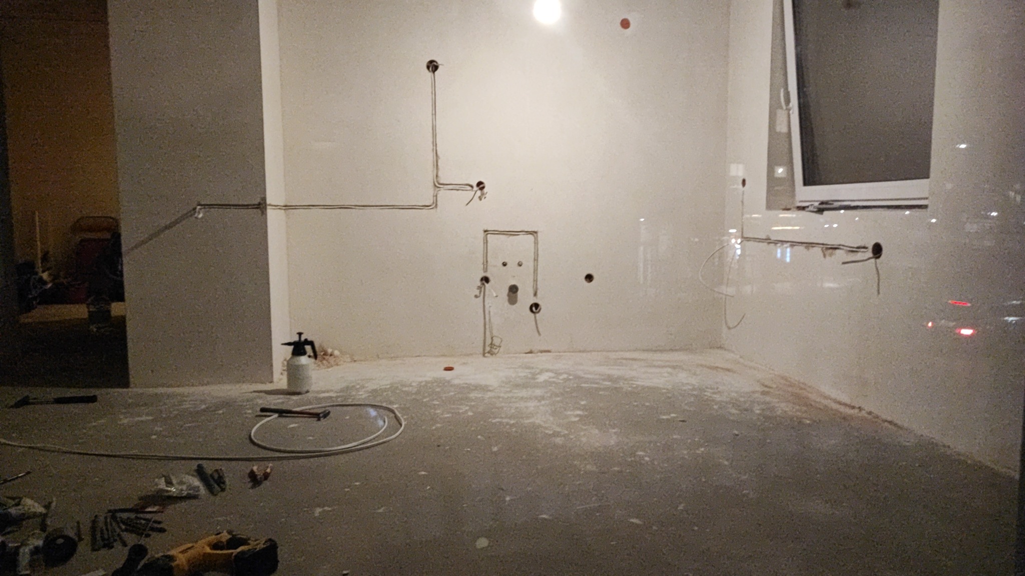 Surowy stan wnętrza z przygotowaną instalacją elektryczną: kable wyprowadzone ze ścian, widoczne otwory pod gniazdka, narzędzia i akcesoria robocze na podłodze, w tle otwarta przestrzeń do innego...